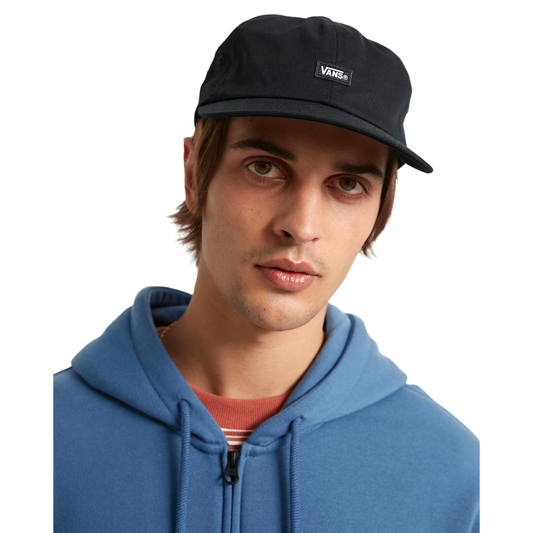 Modelo con Vans Jockey negra puesta, gorra de perfil bajo con visera plana y parche Vans frontal.