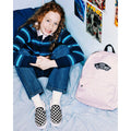 Mochila Vans Old Skool Classic en color pale pink, foto de ambiente junto a una modelo sentada en la cama, mostrando el tono rosa pálido en contexto real.