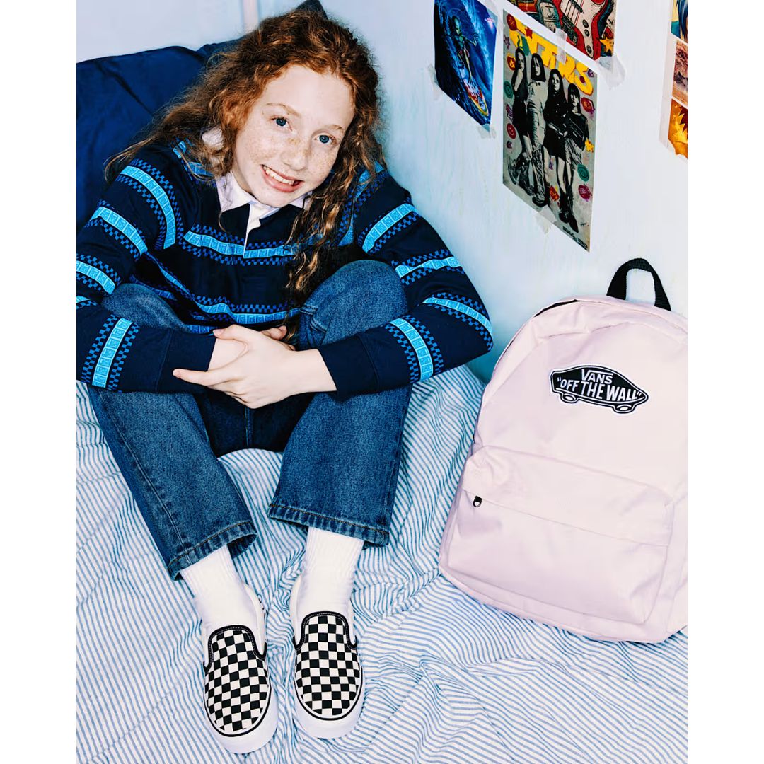 Mochila Vans Old Skool Classic en color pale pink, foto de ambiente junto a una modelo sentada en la cama, mostrando el tono rosa pálido en contexto real.
