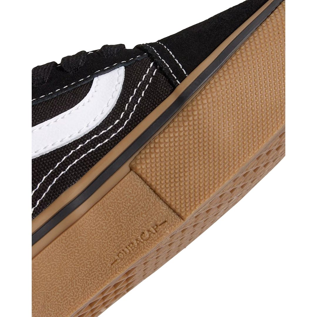 Vans Skate Old Skool en negro con suela gum: detalle macro de la puntera reforzada DURACAP y la textura antideslizante de la suela de goma junto a la franja lateral blanca icónica de la marca.