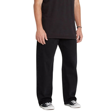 Pantalón vaquero Volcom Billow Denim en negro, vista frontal de perfil sobre modelo con corte ancho, tiro bajo y caída recta hasta el tobillo con zapatillas Converse.