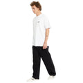 Vaquero ancho Volcom Billow Denim en negro sobre modelo con camiseta blanca, tatuaje visible y zapatillas con estrellas, mostrando el tiro bajo y la caída amplia.