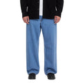 Pantalón vaquero Volcom Billow Denim en azul Cali Blue, vista frontal de cintura para abajo sobre modelo con camisa negra, mostrando el tiro bajo y el corte ancho del pantalón.