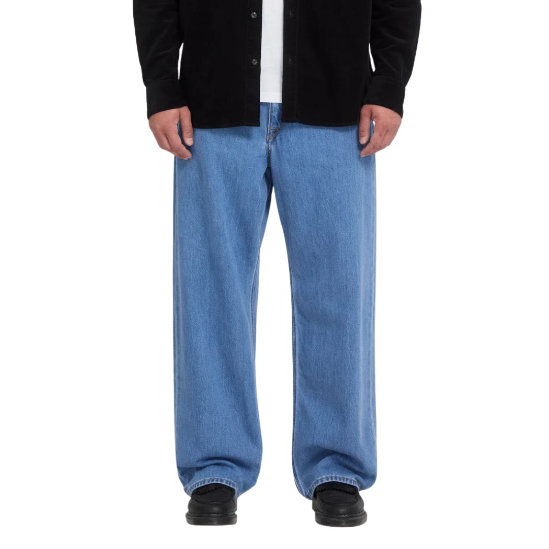 Pantalón vaquero Volcom Billow Denim en azul Cali Blue, vista frontal de cintura para abajo sobre modelo con camisa negra, mostrando el tiro bajo y el corte ancho del pantalón.