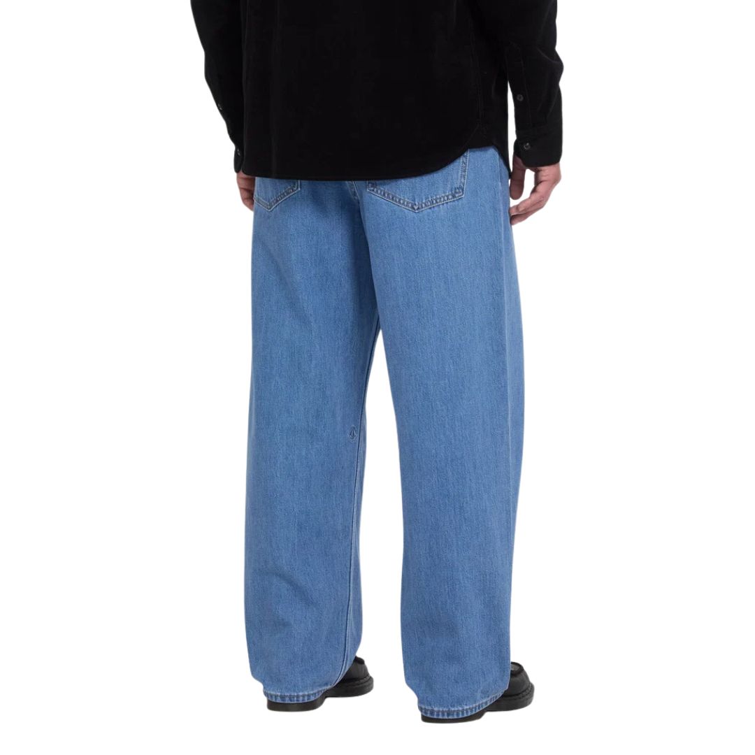 Vaquero ancho Volcom Billow Denim color azul Cali Blue, vista trasera de cintura para abajo con camisa negra, mostrando los bolsillos traseros y la caída recta del pantalón.