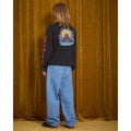 Vaquero Volcom Billow Denim en azul Cali Blue visto de espaldas sobre modelo con camiseta gráfica de manga larga, mostrando el largo y la caída ancha del pantalón hasta el calzado.