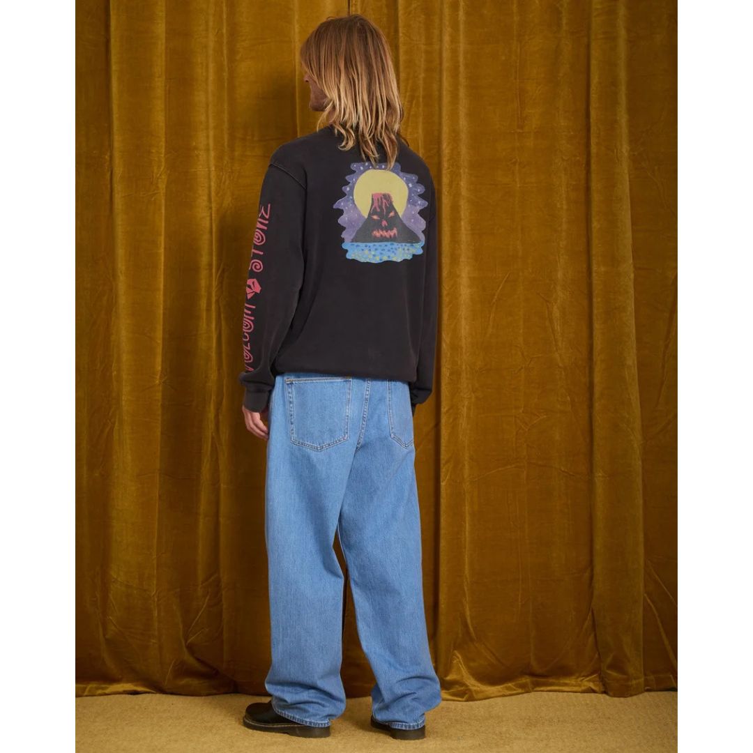 Vaquero Volcom Billow Denim en azul Cali Blue visto de espaldas sobre modelo con camiseta gráfica de manga larga, mostrando el largo y la caída ancha del pantalón hasta el calzado.