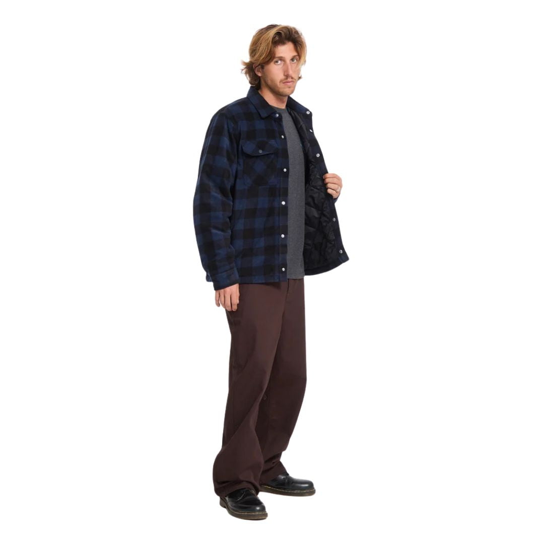Vista lateral de hombre con sobrecamisa Volcom Bowered II en color azul marino a cuadros, sujetando la prenda abierta y mostrando el forro acolchado interior.