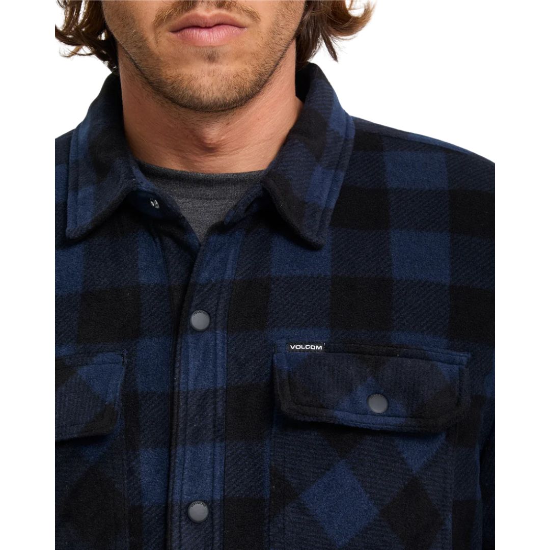 Detalle del cuello y bolsillo con solapa de la sobrecamisa Volcom Bowered II en color azul marino a cuadros, con el adorno metálico de la marca Volcom visible.