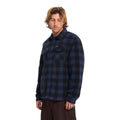 Hombre con sobrecamisa Volcom Bowered II en color azul marino a cuadros en ángulo de tres cuartos, mostrando el bolsillo con solapa y el cierre de botones a presión.