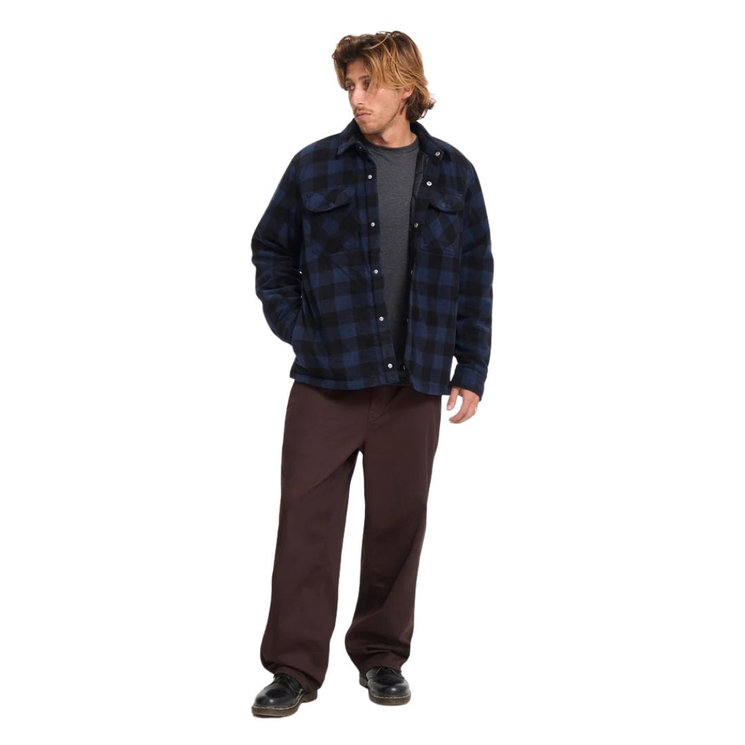 Hombre con sobrecamisa Volcom Bowered II en color azul marino a cuadros de cuerpo entero, con la mano en el bolsillo, luciendo el corte boxy hasta la cadera.
