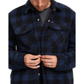 Detalle de hombre abrochando la sobrecamisa Volcom Bowered II en color azul marino a cuadros, con vista cercana de los botones a presión y los bolsillos del pecho.