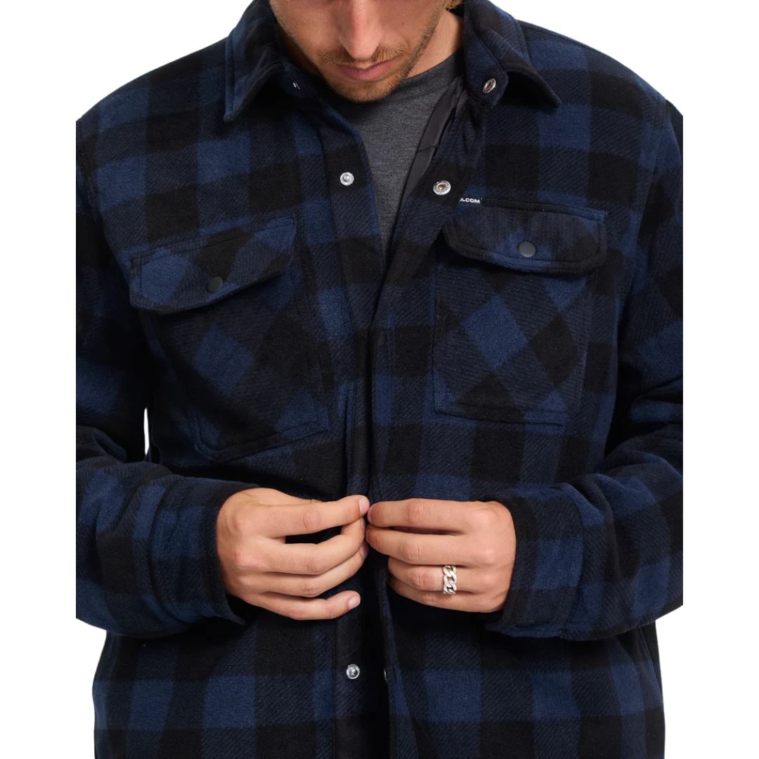 Detalle de hombre abrochando la sobrecamisa Volcom Bowered II en color azul marino a cuadros, con vista cercana de los botones a presión y los bolsillos del pecho.