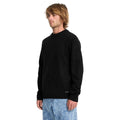 Vista lateral de hombre con jersey Volcom Edmonder II en color negro, mostrando la etiqueta Volcom cosida junto al bajo y el corte normal de la prenda.
