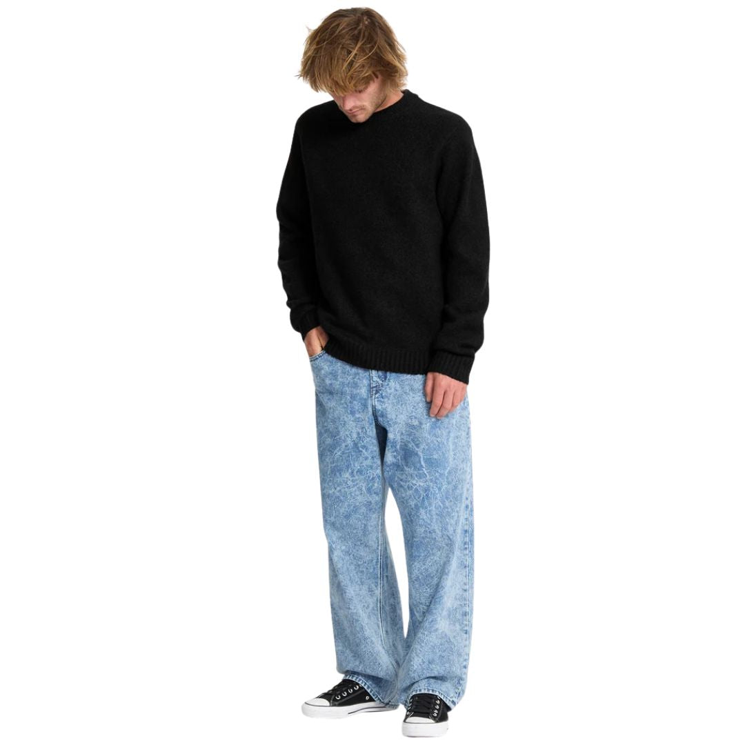 Hombre con jersey Volcom Edmonder II en color negro de cuerpo entero, con la mano en el bolsillo del pantalón, luciendo el corte normal y el largo de la prenda.