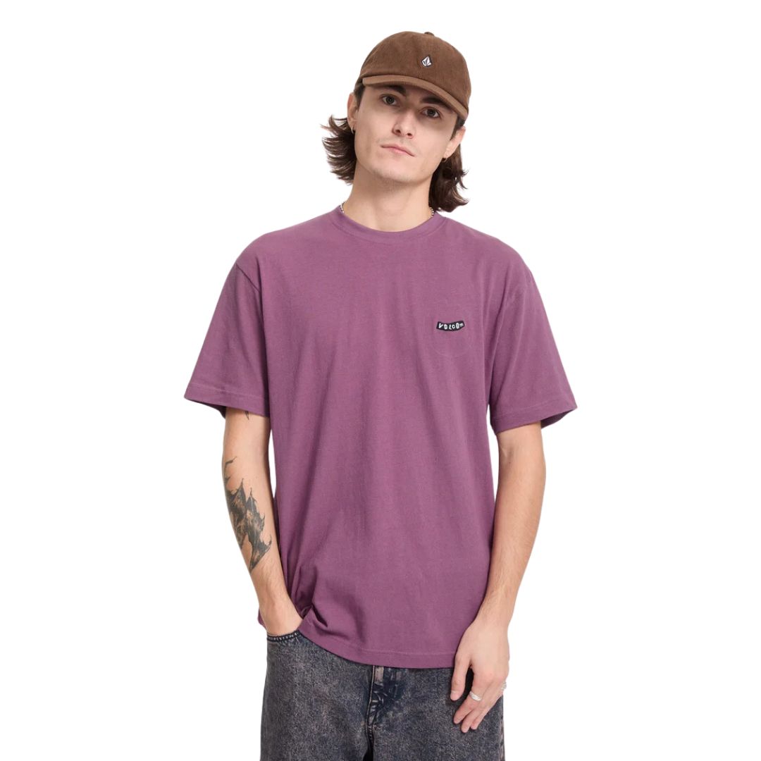 Hombre con gorra Volcom Full Stone Adj Corduroy Cap en color cacao, vista frontal de medio cuerpo combinada con una camiseta de color malva con logo Volcom.