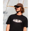 Hombre con gorra Volcom Full Stone Adj Corduroy Cap en color cacao, primer plano en exterior combinada con una camiseta negra con estampado de la marca Volcom.