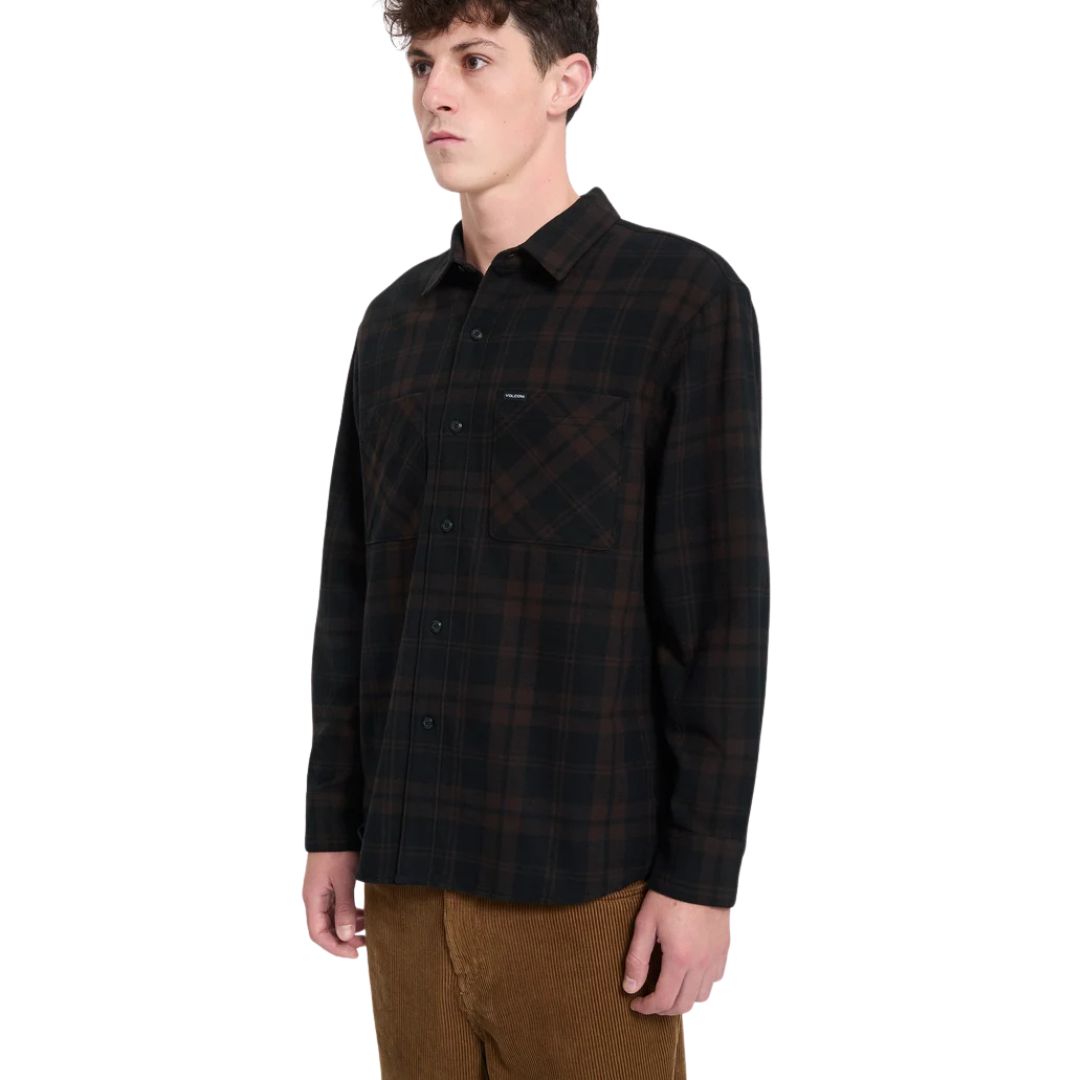 Hombre con camisa Volcom Hunkstone LS en color cacao a cuadros, en ángulo de tres cuartos, mostrando el doble bolsillo en el pecho y el cuello simple de la prenda.