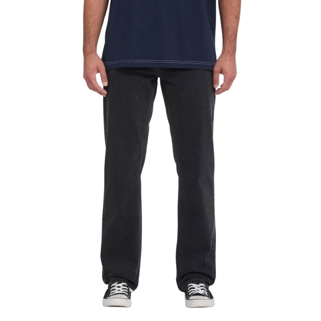 Vaquero Volcom Kinkade Denim en negro lavado, vista frontal de cintura para abajo sobre modelo con camiseta azul marino, mostrando el corte normal y el tiro bajo.