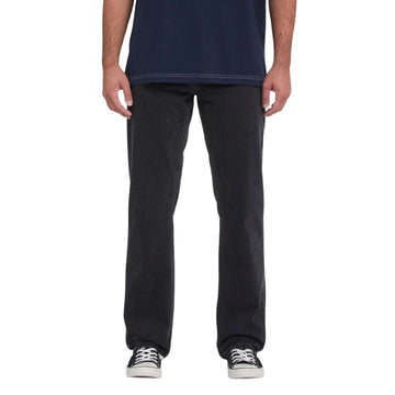 Vaquero Volcom Kinkade Denim en negro lavado, vista frontal de cintura para abajo sobre modelo con camiseta azul marino, mostrando el corte normal y el tiro bajo.