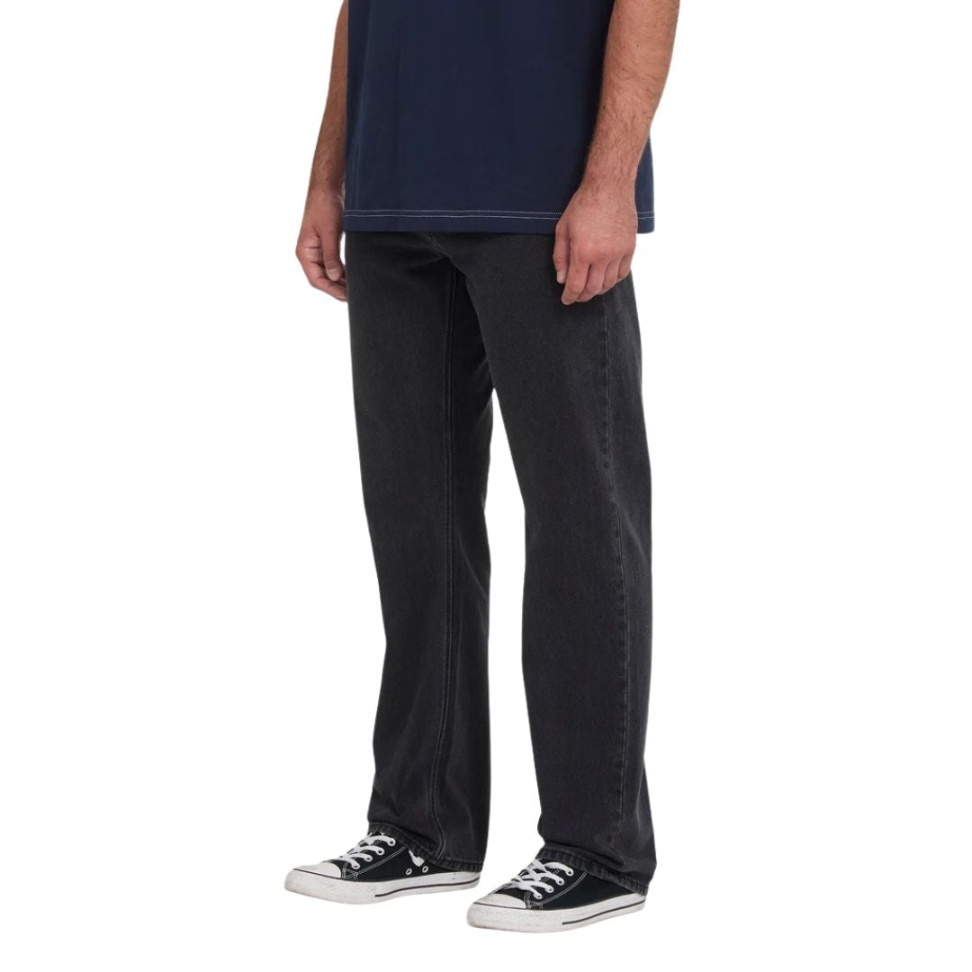 Vaquero recto Volcom Kinkade Denim en negro lavado, vista lateral de cintura para abajo sobre modelo con camiseta azul marino, mostrando la pierna recta y el tiro bajo.