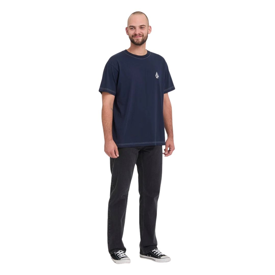 Modelo con pantalón vaquero Volcom Kinkade Denim en negro lavado, vista frontal completa mostrando el tiro bajo y la caída recta hasta el tobillo con zapatillas Converse.
