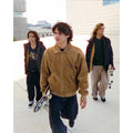 Tres jóvenes caminando con monopatines, el del centro con chaqueta Volcom Kurtis en color armiño, mostrando cómo combina la prenda en un look urbano de skate.
