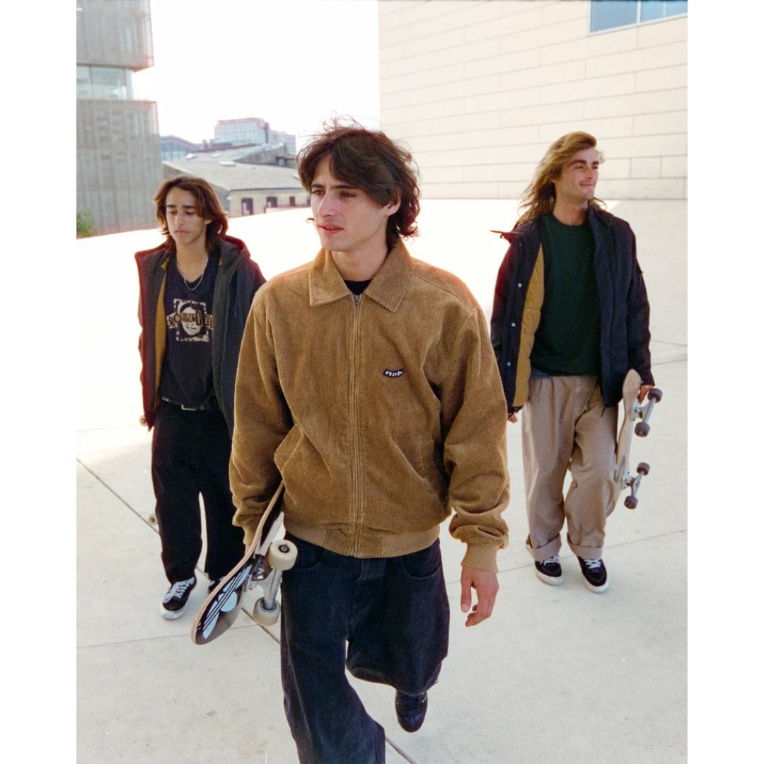 Tres jóvenes caminando con monopatines, el del centro con chaqueta Volcom Kurtis en color armiño, mostrando cómo combina la prenda en un look urbano de skate.