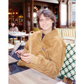 Hombre sonriente con chaqueta Volcom Kurtis en color armiño sentado en una terraza urbana, con la cremallera subida y el logo Volcom visible en el pecho.