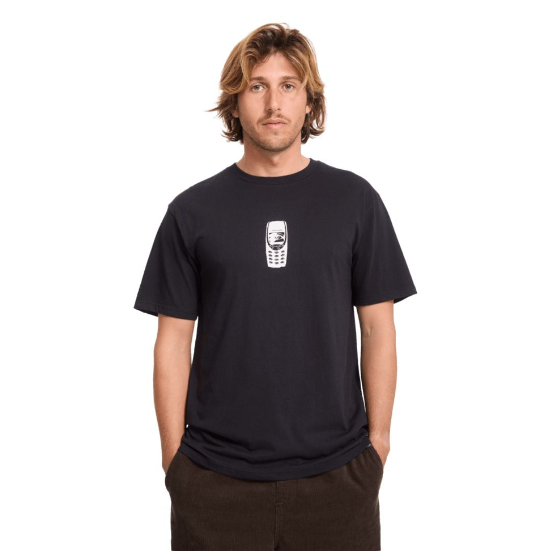 Modelo con la camiseta Volcom Last Call BSC SST en color negro, vista frontal completa mostrando el pequeño estampado del teléfono retro en el pecho y el corte clásico.