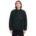 Hombre con sudadera Volcom Muzzer Fuzzar Zip en color verde escarabajo, vista frontal de medio cuerpo mostrando el bolsillo de pecho con cremallera y el cuello alto.