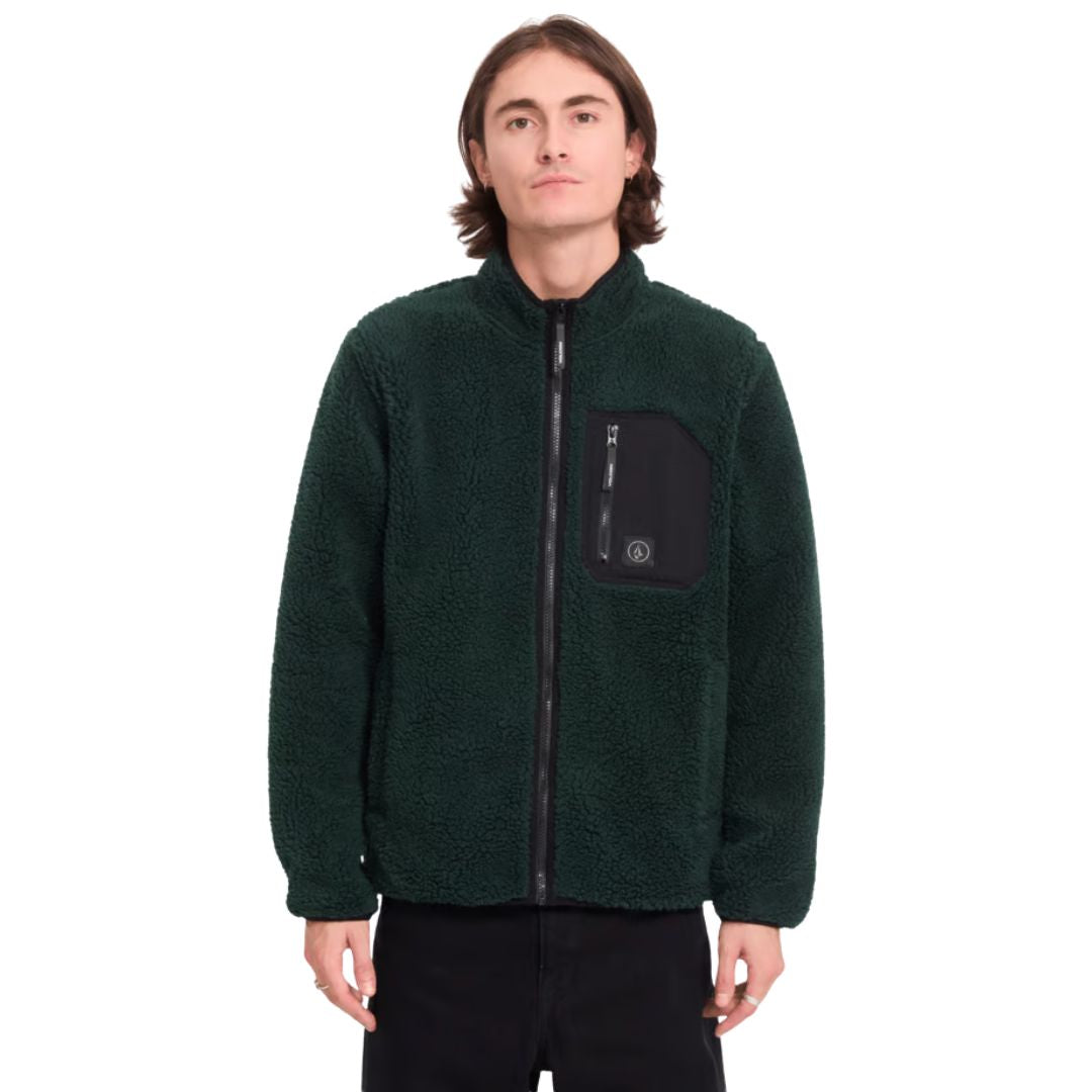Hombre con sudadera Volcom Muzzer Fuzzar Zip en color verde escarabajo, vista frontal de medio cuerpo mostrando el bolsillo de pecho con cremallera y el cuello alto.