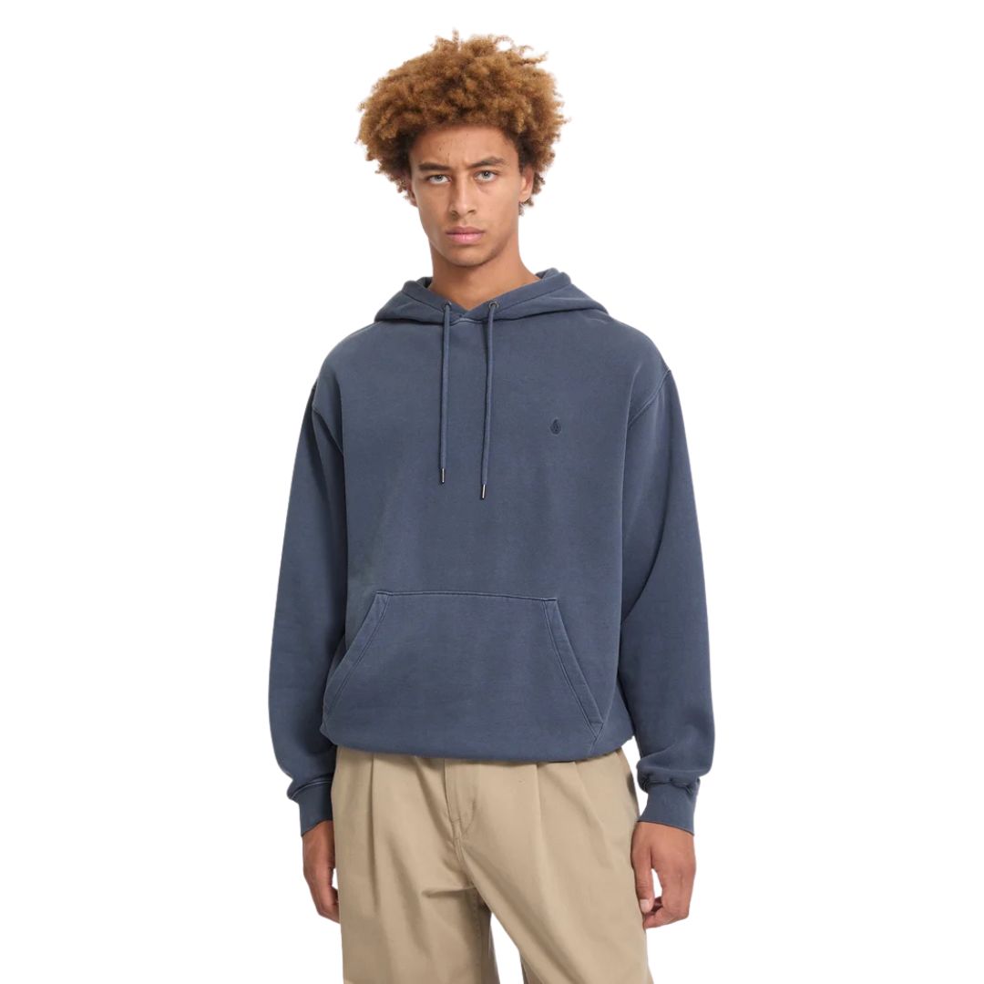 Modelo luciendo la sudadera con capucha Volcom Single Stone PW PO en color storm blue de cuerpo entero, con la capucha sujeta con ambas manos mostrando el ajuste del cordón.