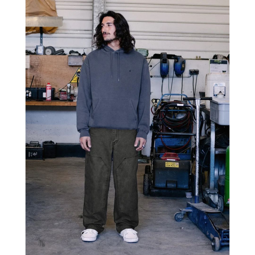 Modelo con la sudadera con capucha Volcom Single Stone PW PO en color storm blue, vista frontal en escena de taller, con la mirada hacia un lado y capucha suelta.