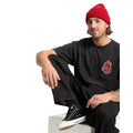 Modelo masculino sentado con camiseta Volcom Snake Peace LSE SST negra y gorro rojo.