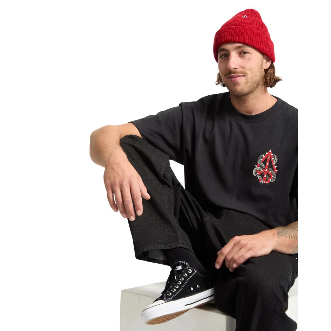 Modelo masculino sentado con camiseta Volcom Snake Peace LSE SST negra y gorro rojo.