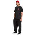 Modelo masculino vistiendo camiseta Volcom Snake Peace LSE SST negra, conjunto completo con gorro rojo y pantalón negro.