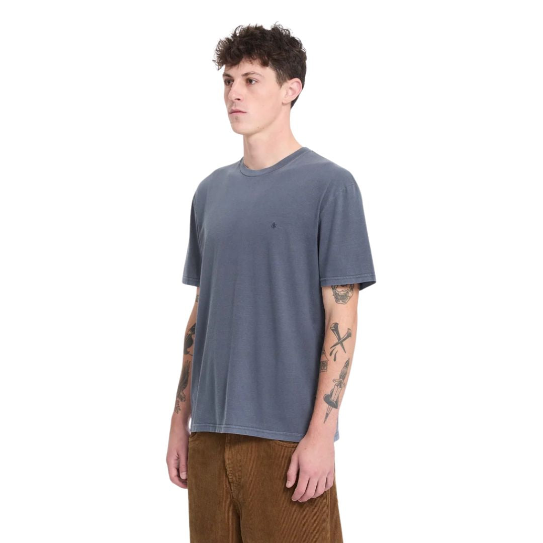 Modelo con la camiseta Volcom Solid Stone EMB SST en color storm blue de cuerpo entero, con gafas de sol y manos en los bolsillos, mostrando el corte y la caída general de la prenda.