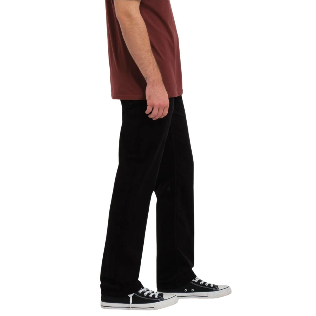Modelo con el pantalón Volcom Solver 5 Pocket Cord en color negro, vista lateral completa caminando, mostrando la caída de la pierna y el calzado a juego.
