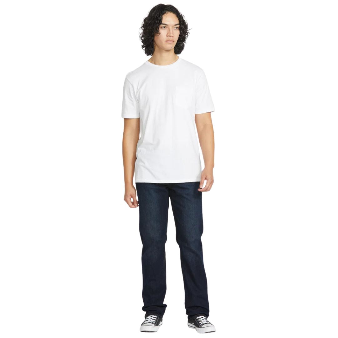Modelo de pie vistiendo pantalón vaquero Volcom Solver Denim color New Washed Blue combinado con camiseta blanca y zapatillas negras.