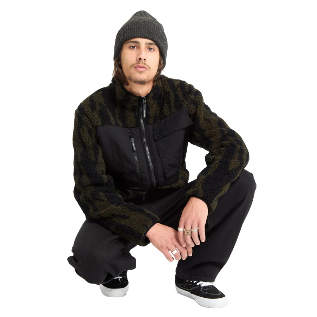 Modelo agachado con chaqueta Volcom Storm Stone Zip verde y camuflaje.