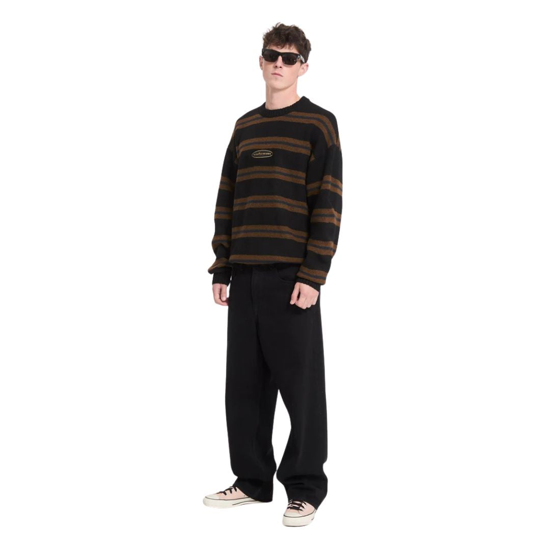 Hombre con gafas de sol y jersey Volcom Striperstand en color negro de rayas, cuerpo entero en ángulo de tres cuartos, luciendo el cuello redondo y el largo del corte amplio.