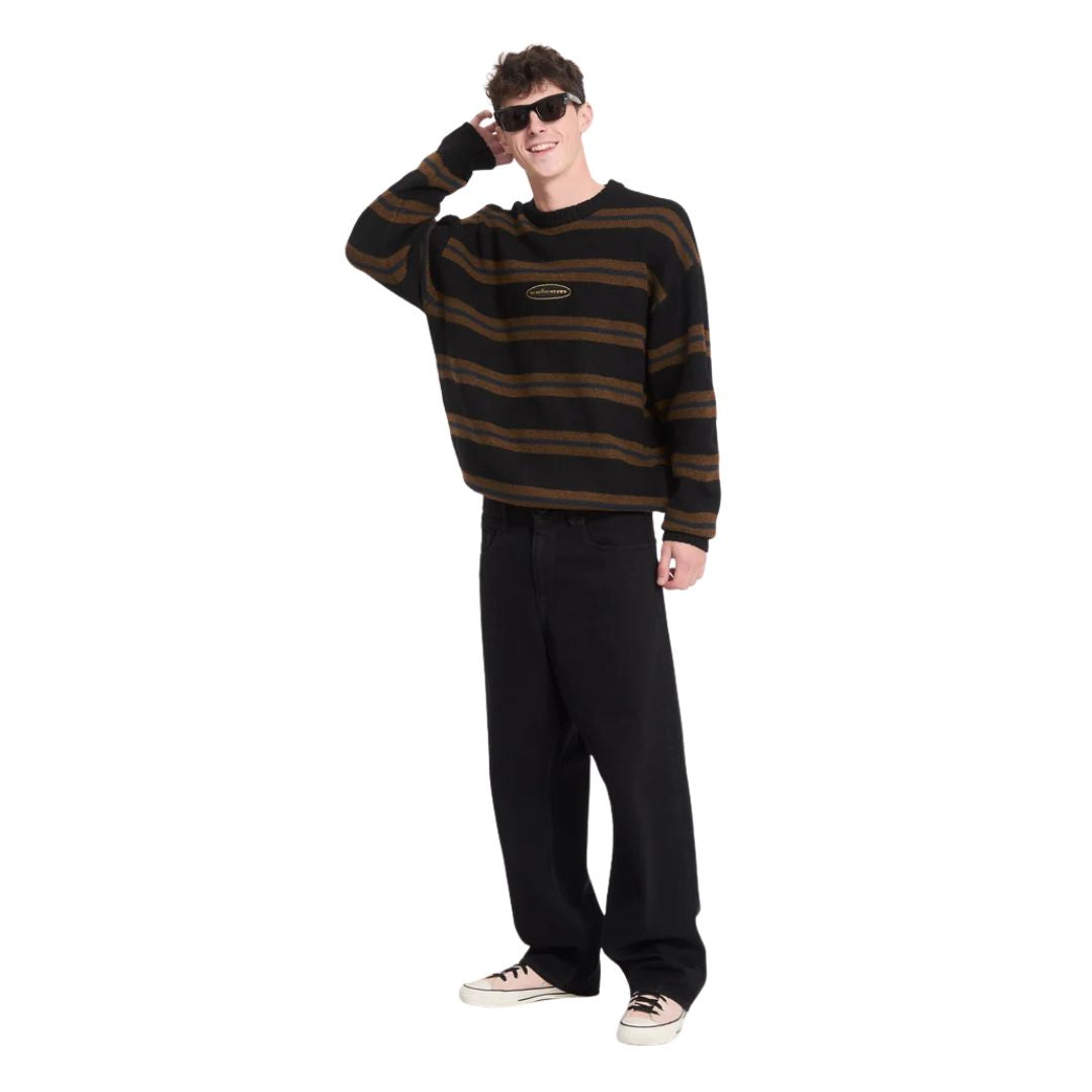 Hombre con jersey Volcom Striperstand en color negro de rayas de cuerpo entero, con la mano en la cabeza, mostrando el corte amplio y el estampado jacquard.