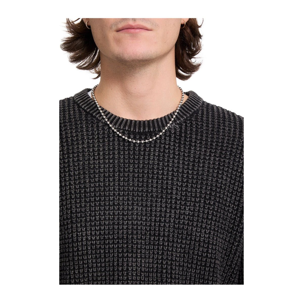 Detalle en primer plano del cuello redondo de canalé y de la textura del punto gofrado del jersey Volcom Thermowhy Sweater negro, sobre el pecho del modelo