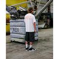 Camiseta Volcom Workwear SST blanco en entorno industrial con estampado trasero naranja.