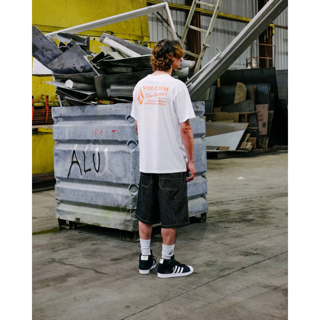 Camiseta Volcom Workwear SST blanco en entorno industrial con estampado trasero naranja.
