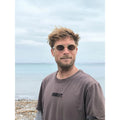 Hombre con gafas de sol Warmouth Grunge Brown de frente, montura ovalada acetato camel con lente marrón, look surfero en la playa.